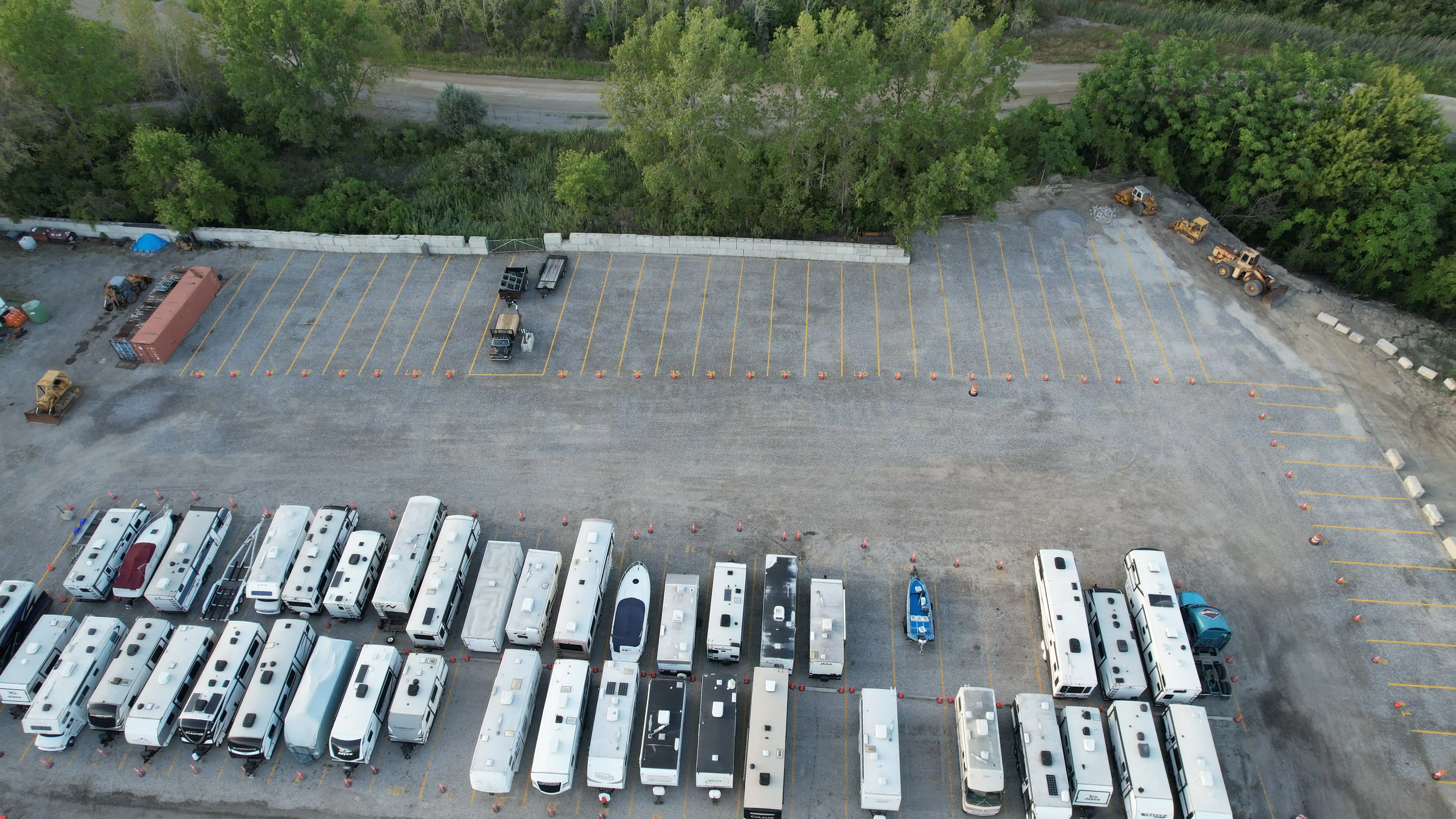 Open pull-thru spaces with yellow striping beside rows of stored RVs, trailers and a boat